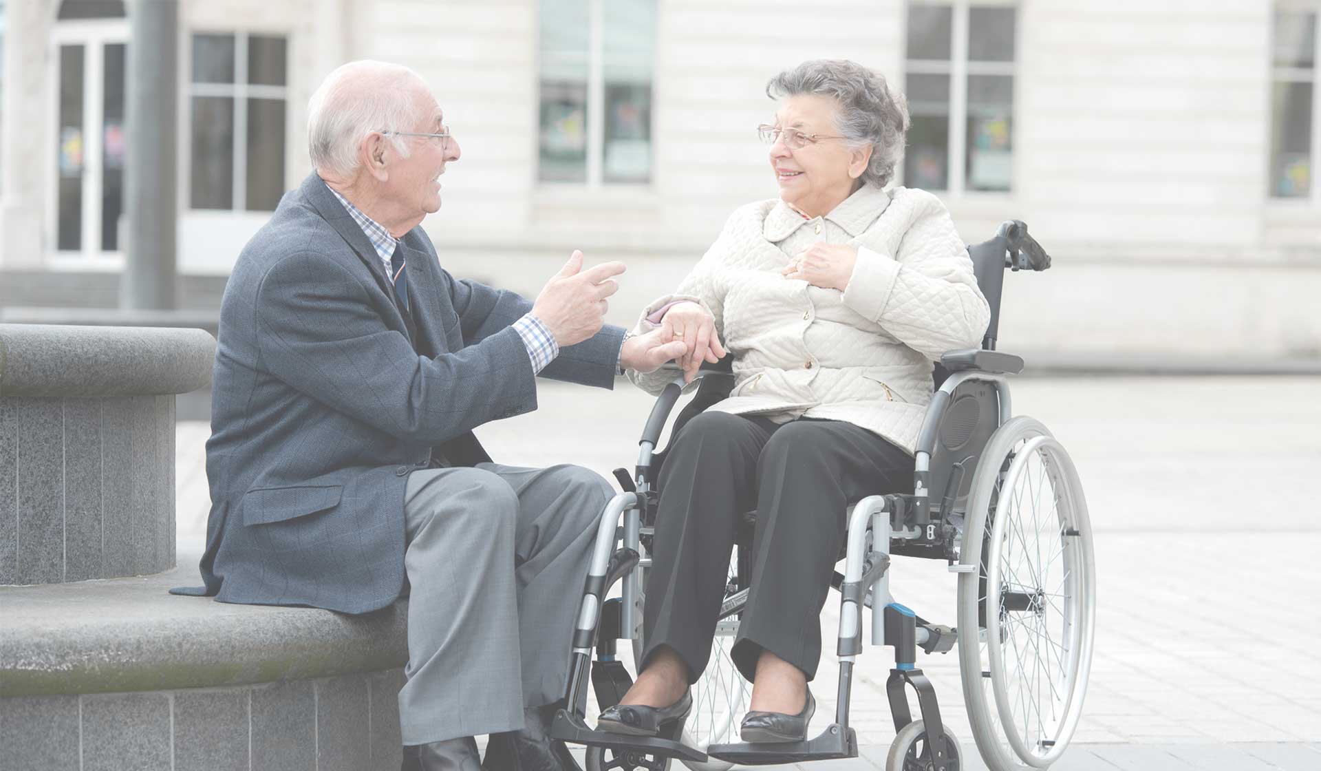 Äldre par samtalar utomhus där den ene sitter i rullstol